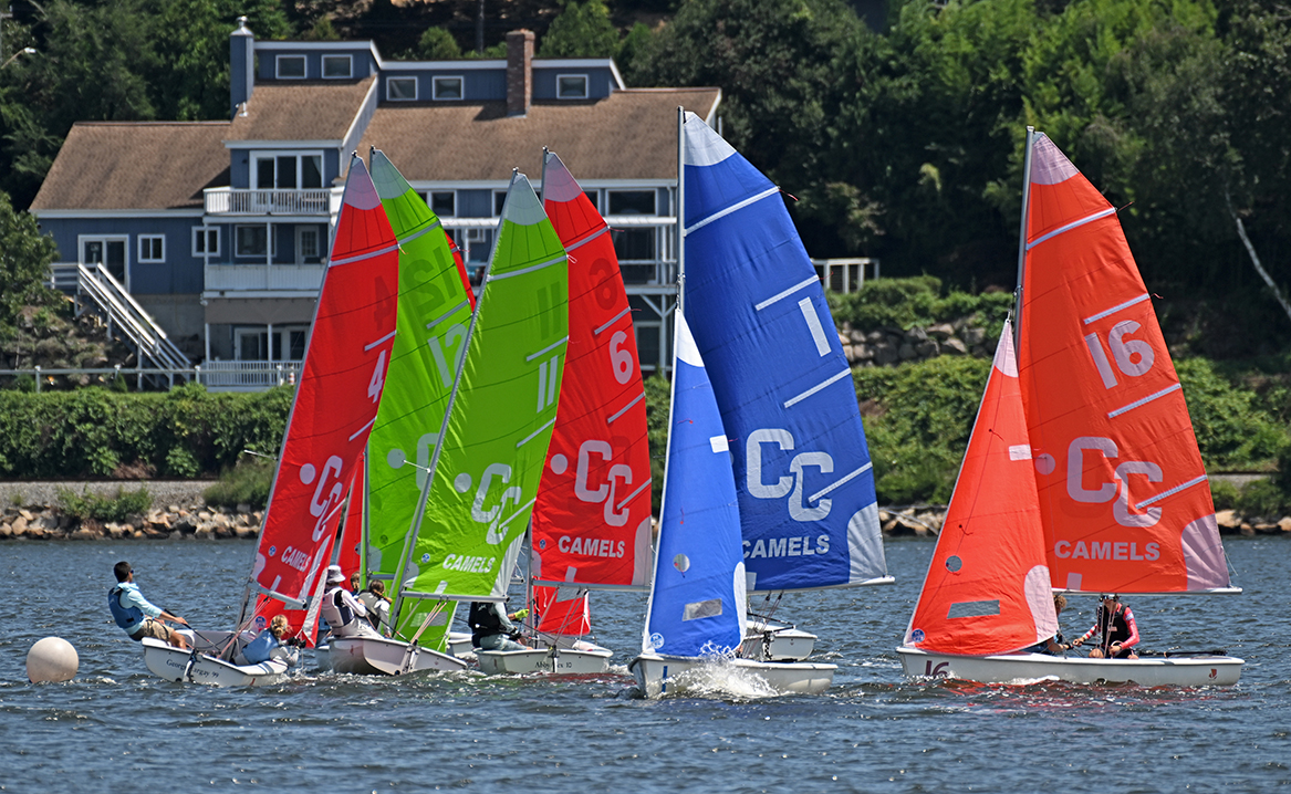 Sailboats with red, green, and blue sails jockey for position at the start of a sailing race