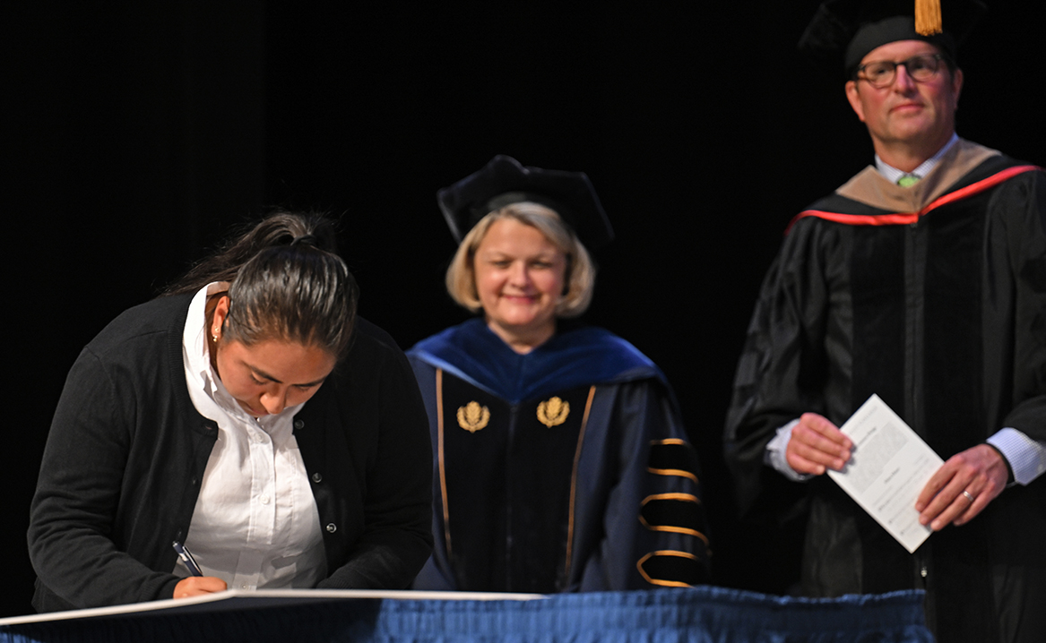 SGA President Bella Castellanos Palacios ’25 signs the Shared Governance Covenant as President Chapdelaine and BOT Chair Seth Alvord ’93 look on.