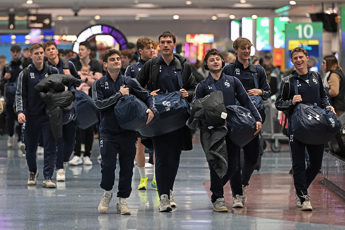 A group of soccer players walk through an airport baggage claim area.