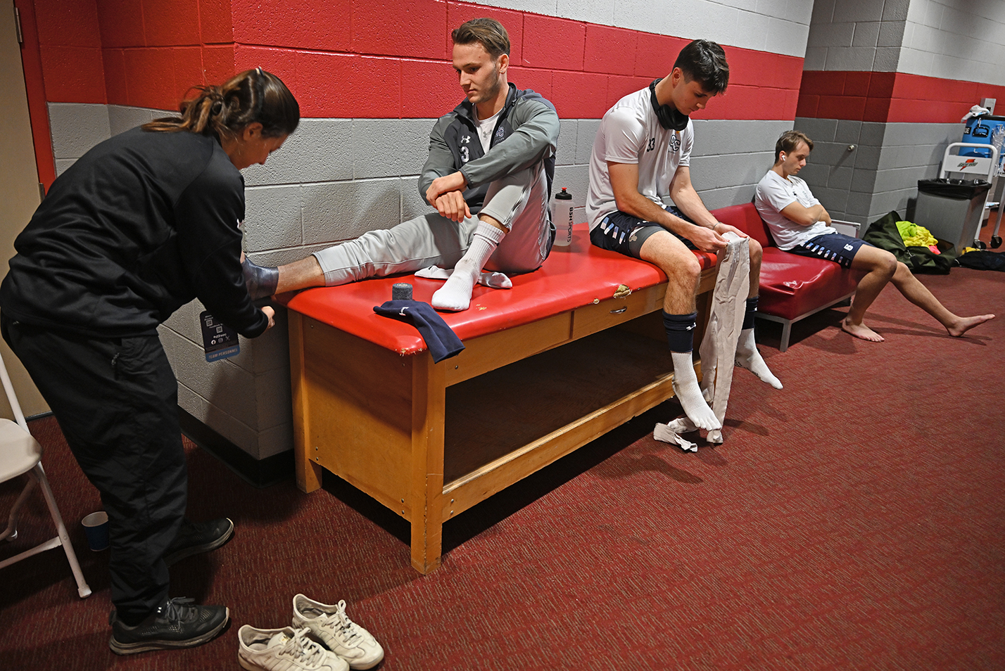 An athletic trainer tapes the ankle of one soccer player while other await treatment.