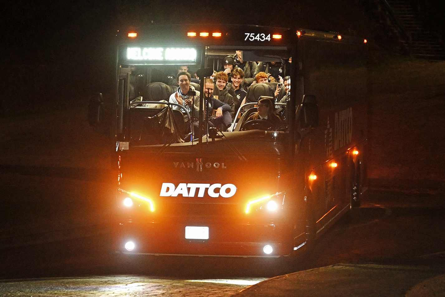 A smiling soccer team looks out into the dark as their bus arrives home.