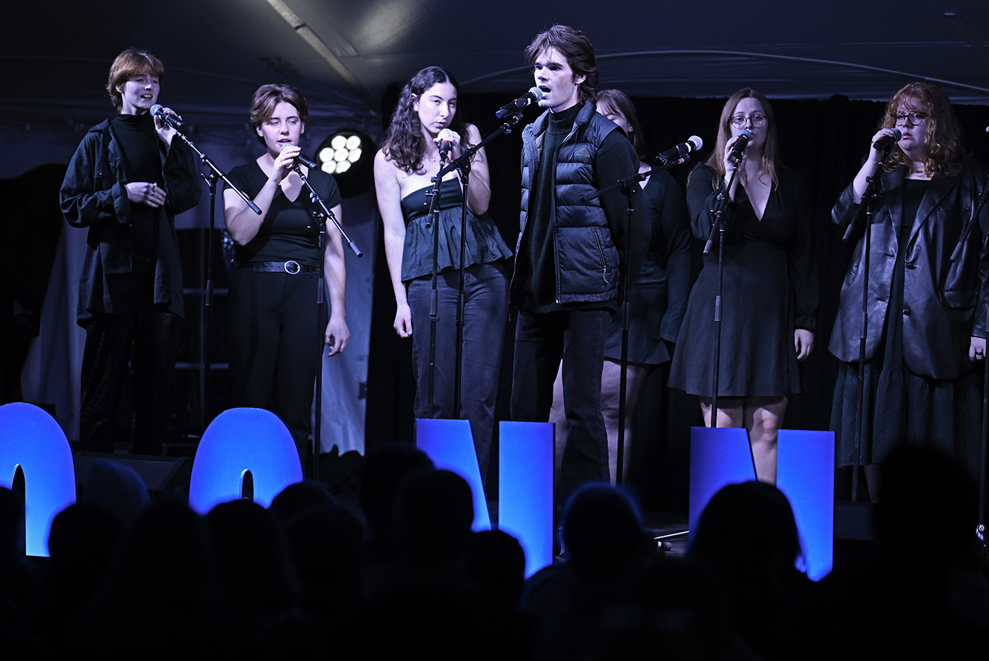 An a cappella group, dressed in black, performs on stage.