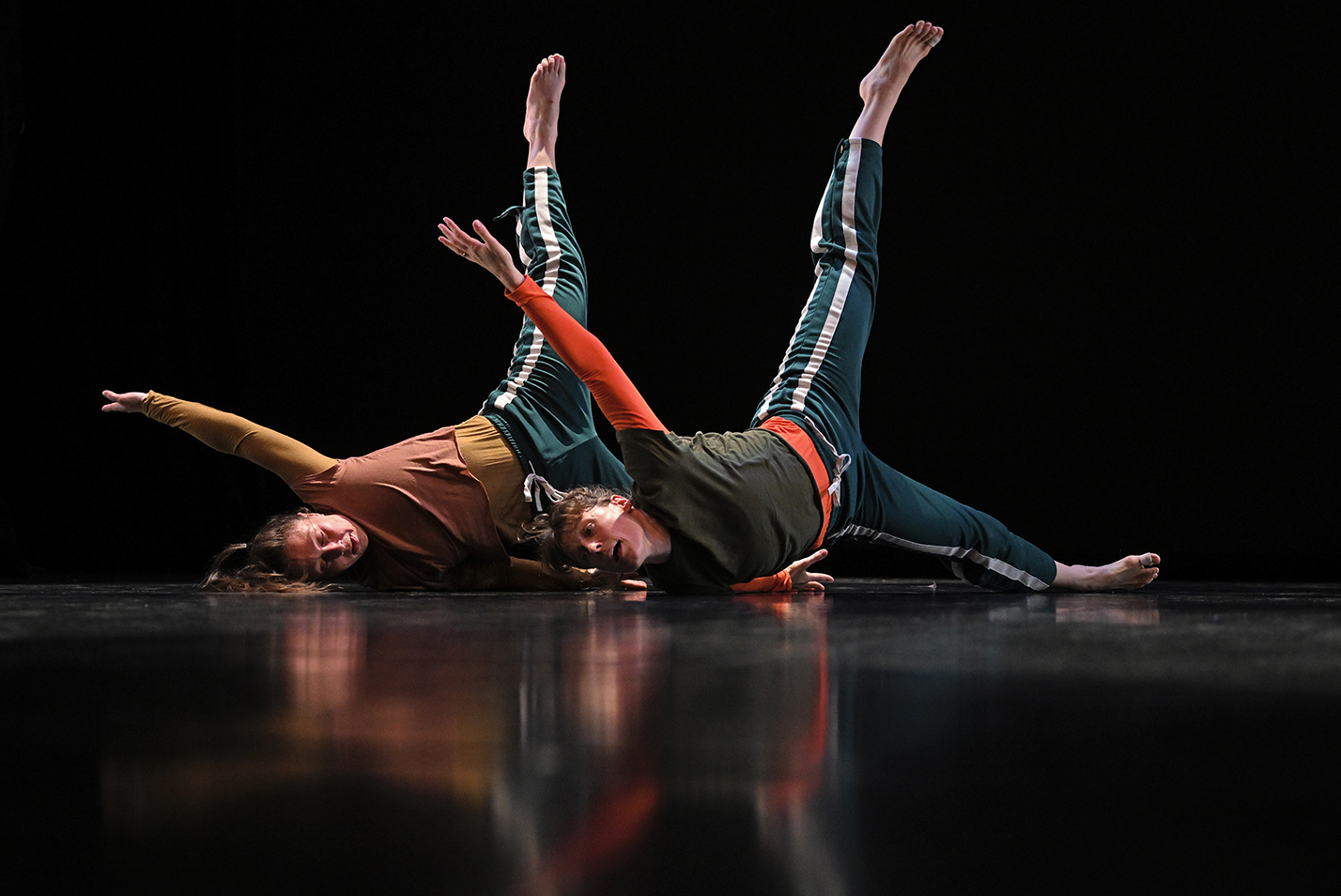 two dancers, on their sides on the floor with one are and one leg each in the air, perform on stage