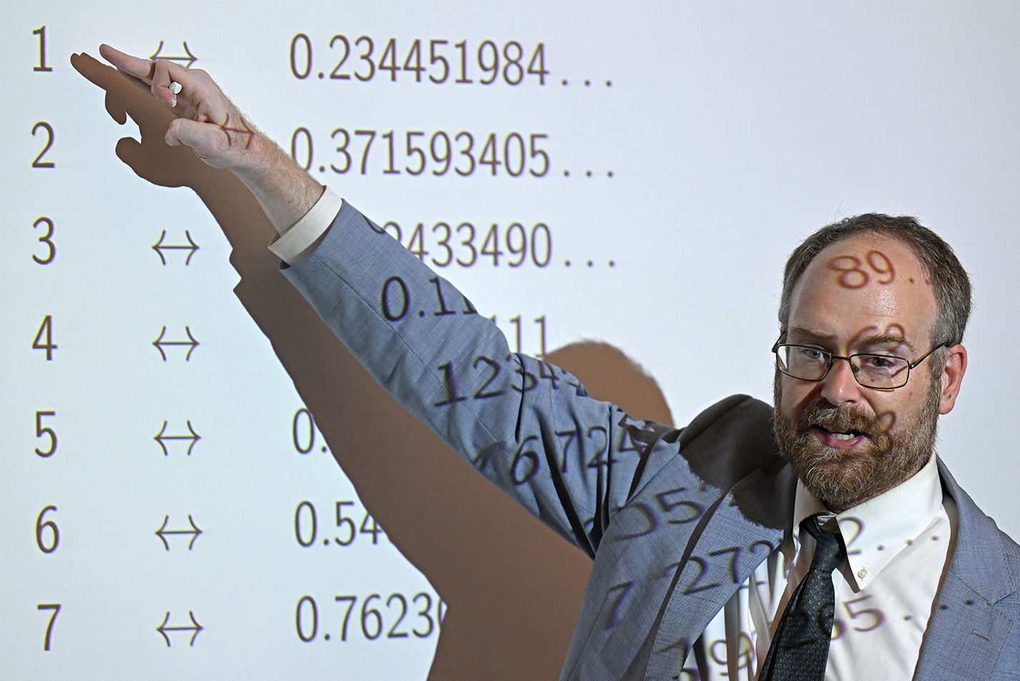 A mathematics professor has numbers projected on his face as he explains an equation to students.