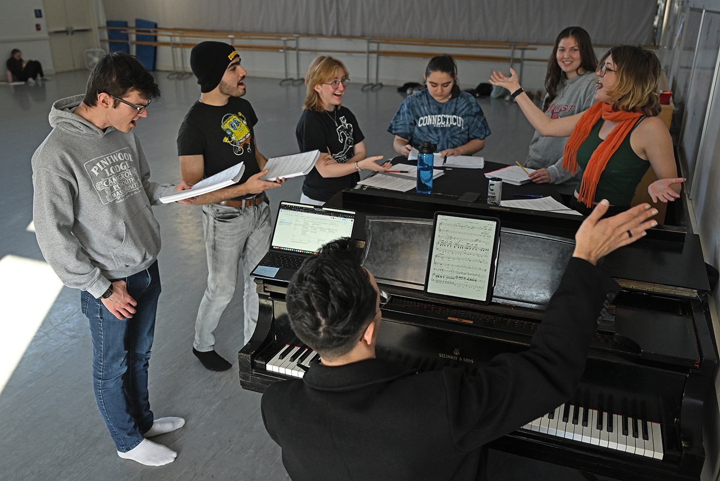 Actors gather around a piano to rehearse a number for a musical theater production.